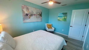 A bedroom with a bed, a chair, and artwork on the walls. - Chill Vibes A - 2 min to Beach (Fort Myers Beach)