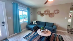 A living room with a teal sofa, a patterned rug, and wall decor. - Chill Vibes B - 2 min to Beach (Fort Myers Beach)