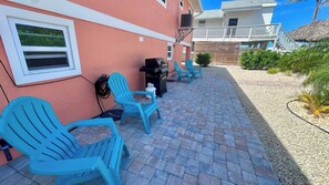 A patio area with blue chairs, a grill, and a poolside deck. - Chill Vibes B - 2 min to Beach (Fort Myers Beach)