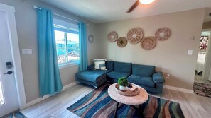 Ein Wohnzimmer mit einem blauen Sofa, einem runden Couchtisch mit einer Pflanze, einem Streifen Teppich und Wanddekoration.