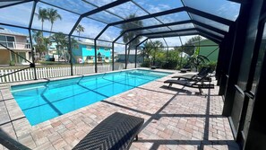 A swimming pool with a glass enclosure, surrounded by lounge chairs and a brick patio. - Chill Vibes B - 2 min to Beach (Fort Myers Beach)