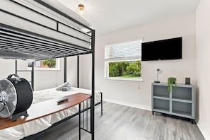 Une chambre moderne avec un lit superposé, un bureau avec un ventilateur, une télévision et une étagère grise.