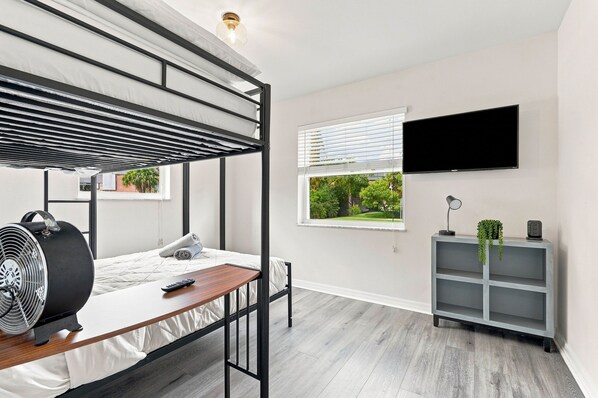 Un dormitorio moderno con una litera, un escritorio con un ventilador, un televisor y un estante gris.