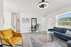 A spacious living room with a yellow armchair, a blue sofa, and a large window with a view of greenery. - West Palm Beach 3BR Luxury Home Near Beach&Dining (West Palm Beach)