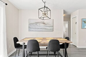A dining area with a wooden table, four chairs, a hanging geometric light fixture, and a wall-mounted abstract painting. - West Palm Beach 3BR Luxury Home Near Beach&Dining (West Palm Beach)