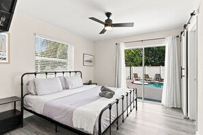 A bedroom with a bed, a ceiling fan, a window with blinds, and a view of a pool area. - West Palm Beach 3BR Luxury Home Near Beach&Dining (West Palm Beach)