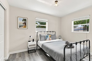 A bedroom with a bed, bedside table, lamp, and two windows. - West Palm Beach 3BR Luxury Home Near Beach&Dining (West Palm Beach)
