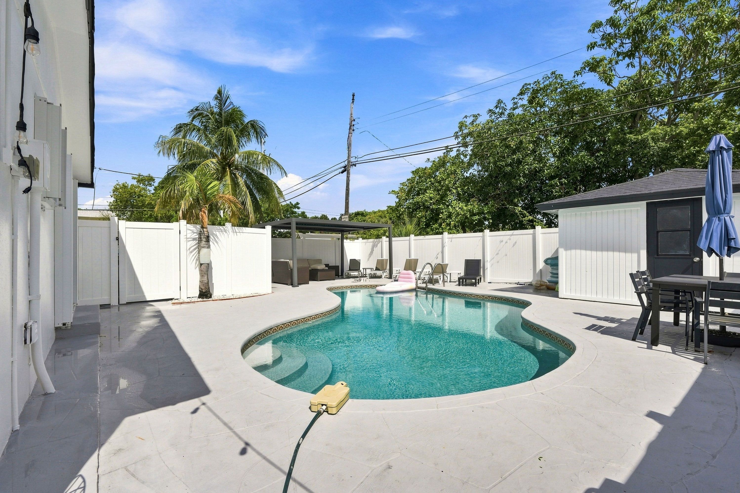 Un jardin avec une piscine, un patio couvert et un espace clos aménagé avec du mobilier d’extérieur.