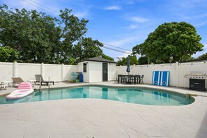 Una piscina con cubierta blanca, un cobertizo pequeño, una parrilla y mobiliario de exterior.