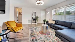 A modern living room with a sofa, a yellow chair, a coffee table, and a large window with blinds. - West Palm Beach 3BR Luxury Home Near Beach&Dining (West Palm Beach)