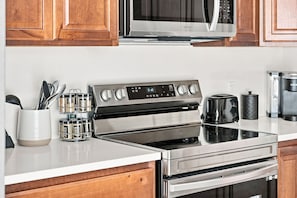 Une cuisine équipée d’une cuisinière en acier inoxydable, d’un four à micro-ondes placé au-dessus et d’une machine à café posée sur le plan de travail.