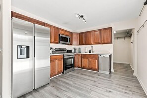 A modern kitchen with wooden cabinets, stainless steel appliances, and a grey wooden floor. - West Palm Beach 3BR Luxury Home Near Beach&Dining (West Palm Beach)
