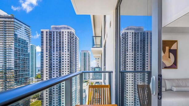 Ein Balkon mit Blick auf hohe Gebäude, einer gepolsterten Sitzecke und einem Bild an der Wand.