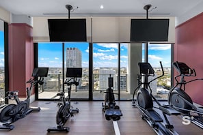 Ein Fitnessstudio mit Ergometer, Laufbändern und einem großen Fenster mit Blick auf die Stadt.
