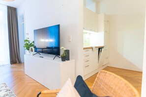 A modern living room with a flat-screen TV, a white entertainment unit, a dining area with a wooden table, and a large window. - Schönbrunn in 10 min cozy&modern (Vienna)