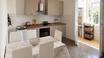 Une cuisine moderne avec des meubles blancs, une table à manger avec des chaises et, vue par une porte ouverte, un balcon.
