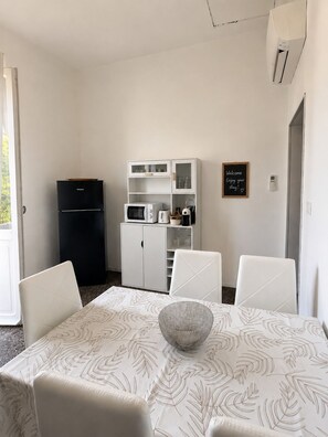 A compact kitchen with a refrigerator, microwave, and cabinets. There is a dining table with four chairs and a decorative bowl. A welcome sign is on the wall. - INDEPENDENT APARTMENT WITH PRIVATE GARDEN AND PERGOLA - DOG FRIENDLY (Valle di Vado)