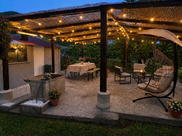 An outdoor patio with tables, chairs, a hanging chair, and string lights. - INDEPENDENT APARTMENT WITH PRIVATE GARDEN AND PERGOLA - DOG FRIENDLY (Valle di Vado)