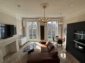 Ein modernes Wohnzimmer mit einem großen Flachbildfernseher, einer Couch, einem Glastisch und einem Essbereich mit Stühlen.