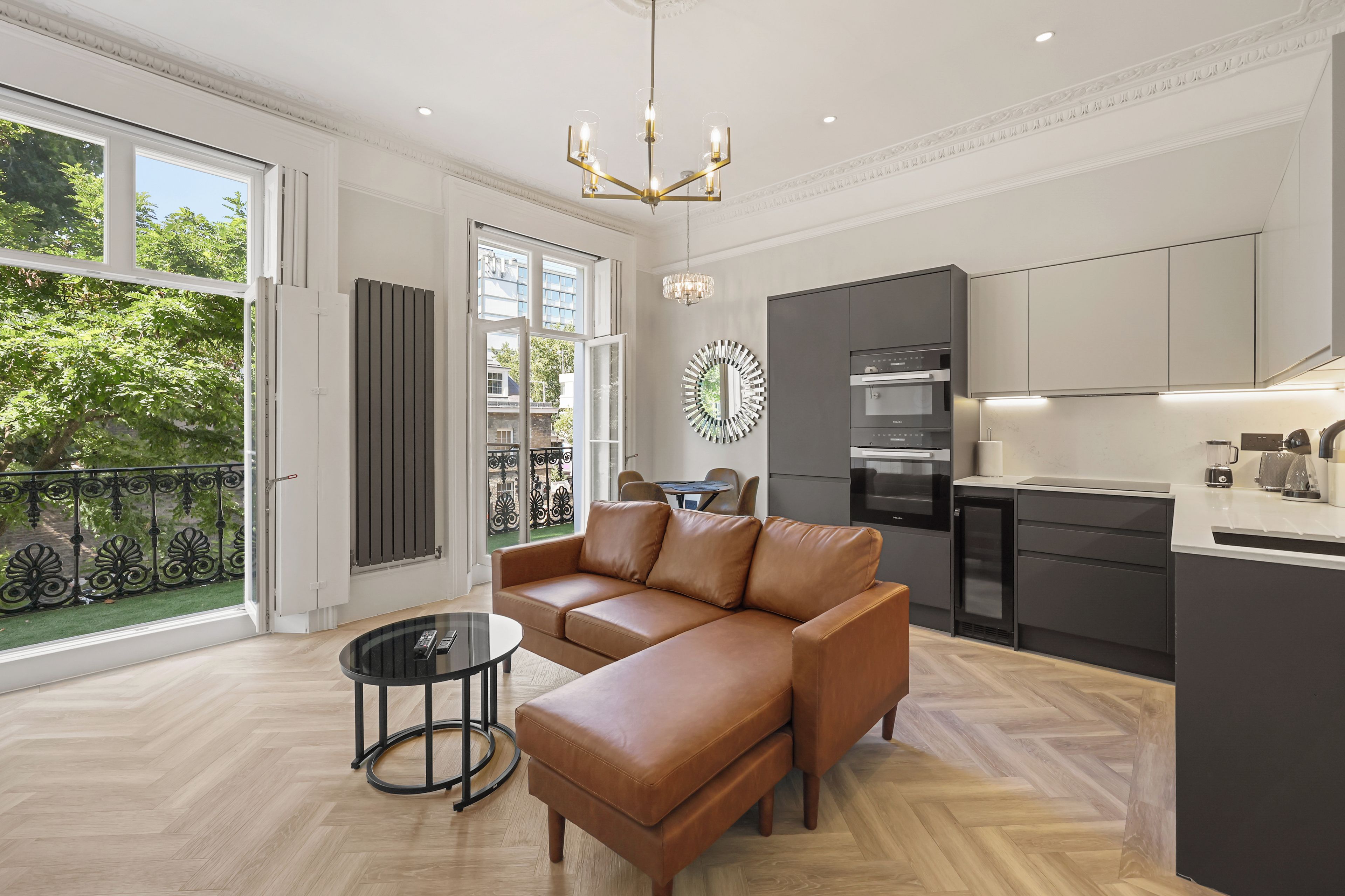 A modern kitchen with built-in appliances, a dining area with a round table, and a living room with a leather sofa and a coffee table.