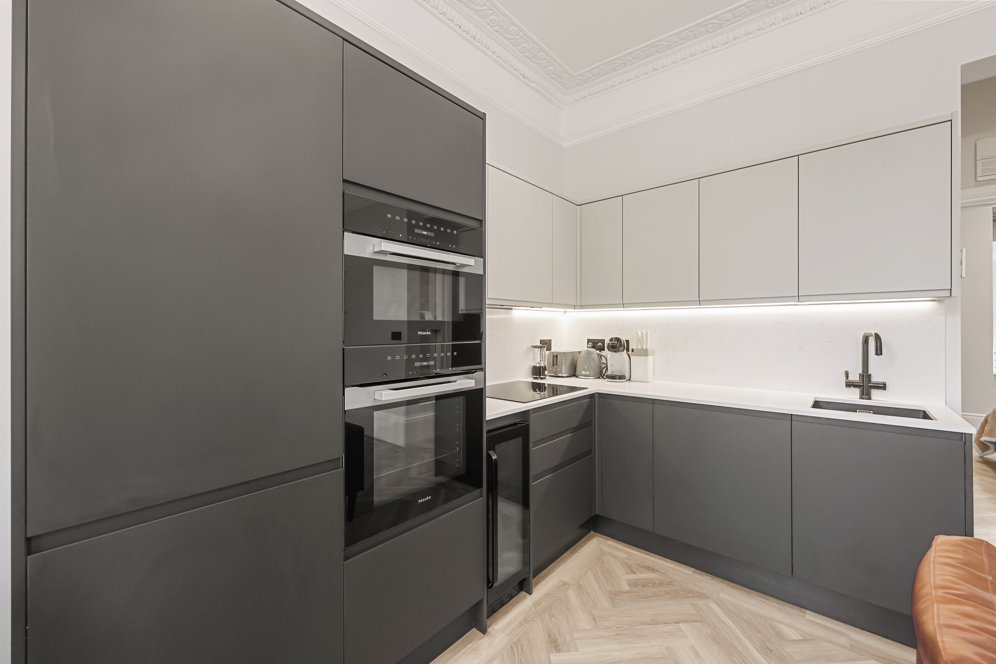A modern kitchen with built-in appliances, a countertop, and a wooden floor.
