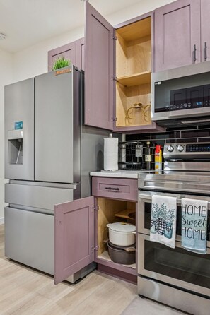 Eine moderne Küche mit Edelstahlgeräten, einem violetten Schrank und einer Kücheninsel.