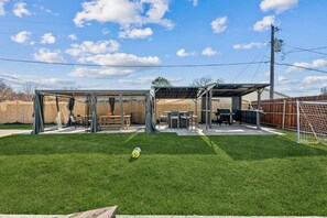 Ein Garten mit überdachter Terrasse, Grill und Fußballtor.