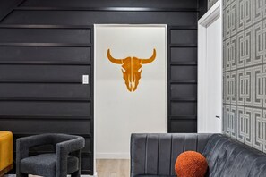 Et moderne interiør med sort-hvid farveskema, billedkunst med en oksehovedskal, en grå sofa med en orange pude og en mønstret væg.