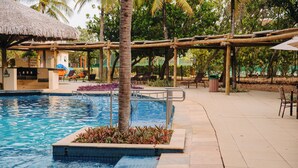 Une piscine dotée d’une structure de toit en chaume, de palmiers et de chaises longues.