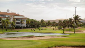 Un parcours de golf doté de bunkers, d’un étang, de palmiers et d’un bâtiment surmonté d’une tour.