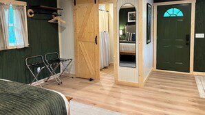 A room with a bed, a wooden door, a sliding barn door, a mirror, and a window with curtains. - Waterfront Cabin in Hilliard, FL (Hilliard)
