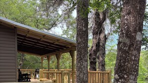 A wooden deck with railings, a covered area, and a view of a body of water. - Waterfront Cabin in Hilliard, FL (Hilliard)