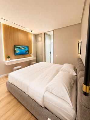 A modern bedroom with a large bed, a TV mounted on a wooden panel, and a glass door leading to a bathroom. - Luxury Apartament (Tiranë)