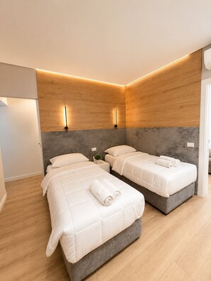A modern hotel room with two beds, a grey headboard, wooden panel walls, and a small bedside table with a plant. - Luxury Apartament (Tiranë)