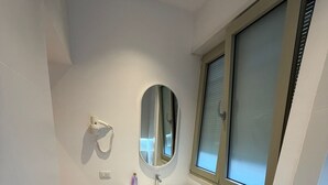 A bathroom with a white sink, a mirror, a hairdryer, and a window. - Luxury Apartament (Tiranë)