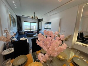 Ein modernes Wohnzimmer mit einer Couch, einem Esstisch für zwei Personen und einem großen Fenster mit Blick auf die Stadt.