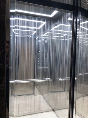 Ein moderner Aufzug mit spiegelnden Glaswänden und geometrischen Leuchten.
