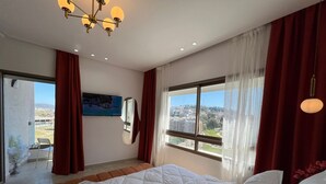 A bedroom with a bed, a large window, a ceiling light fixture, and a painting on the wall. - 2-bedroom apartment in adorable Tangier with AC comfort (Tangier)