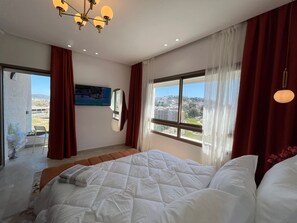 Ein Schlafzimmer mit Bett, großem Fenster, Deckenleuchte und einem Bild an der Wand.