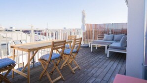 A wooden deck with a table and chairs, a sofa, and a white railing. - Maisonette apartment by Schönbru (Vienna)