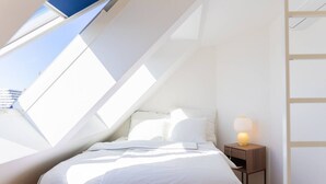 A bedroom with a skylight, a bed, a bedside table with a lamp, and a wooden floor. - Maisonette apartment by Schönbru (Vienna)