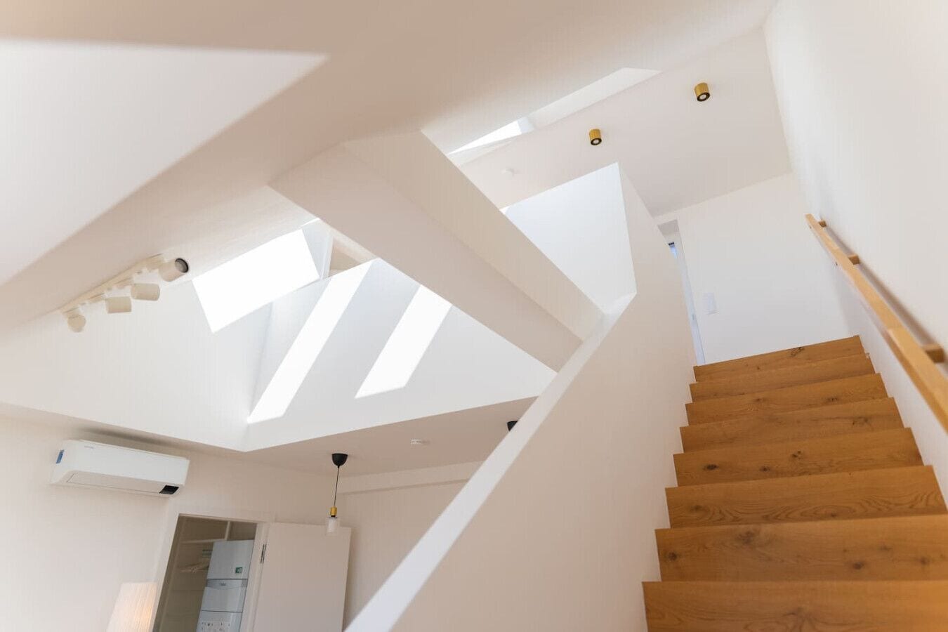 A modern staircase with wooden steps and white walls, leading to a room with skylights.