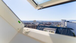 A view from a window with a skylight, overlooking a cityscape with buildings and distant mountains. - Maisonette apartment by Schönbru (Vienna)