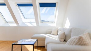 A modern living room with a sofa, a glass coffee table, and skylights. - Maisonette apartment by Schönbru (Vienna)