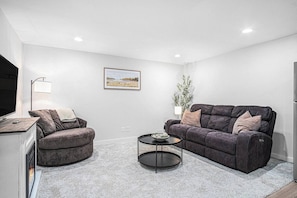 Ein modernes Wohnzimmer mit Sofa, Sessel, Couchtisch und einem Bild an der Wand.