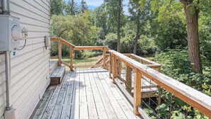 Une terrasse en bois avec des garde-corps, un coffret électrique et une vue sur une zone boisée.