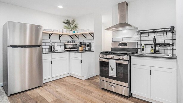 Une cuisine moderne dotée d’appareils électroménagers en acier inoxydable, de meubles blancs et d’un plancher en bois.