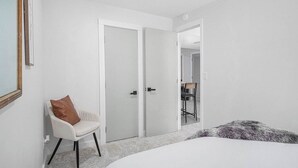 Une chambre à coucher comprenant un lit, une chaise, une armoire et une porte donnant sur une autre pièce.