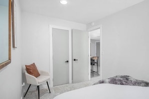 Een slaapkamer met een bed, een stoel, een kast en een deur naar een andere kamer.