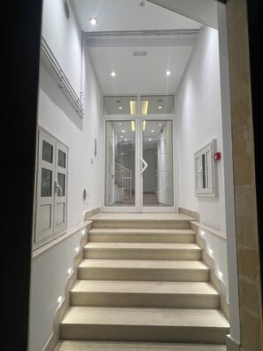Una escalera conduce a un rellano con puertas de vidrio, paredes blancas e iluminación empotrada.
